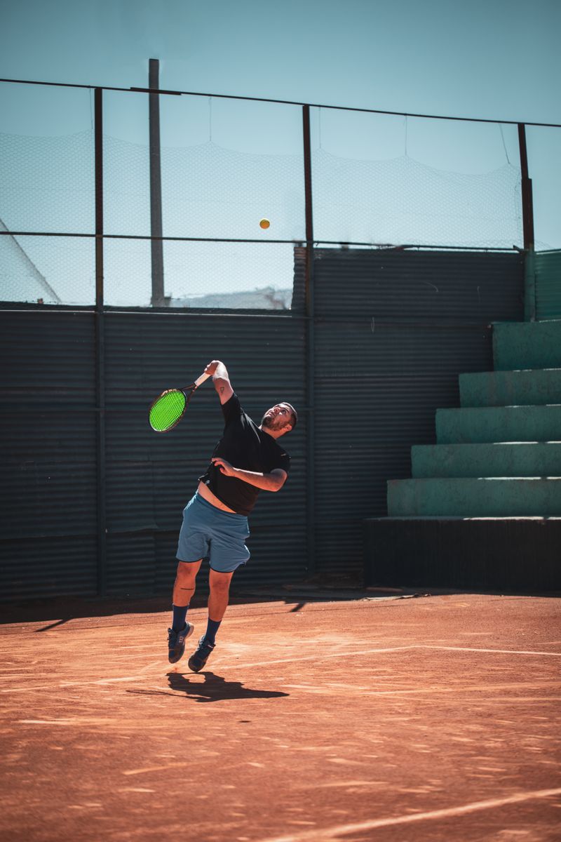 Jugador de tenis en pleno saque sobre una cancha de polvo de ladrillo
