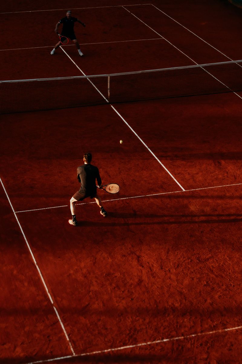 Partido de tenis al atardecer en una cancha de polvo de ladrillo
